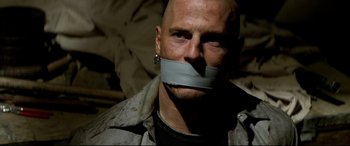 Movie still from “xXx” (2002), directed by Rob Cohen – A bald man with a gray duct tape over his mouth; Close Up shot, Over the shoulder angle