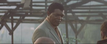 Movie still from “xXx” (2002), directed by Rob Cohen – A man wearing a suit and tie standing in front of a building; Close Up shot, Low angle