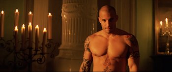 Movie still from “xXx” (2002), directed by Rob Cohen – A man with tattoos is standing in front of candles; Medium shot, Over the shoulder angle