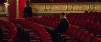 Movie still from “xXx” (2002), directed by Rob Cohen – A man sitting alone in a theater with his hands clasped together; Wide shot, High angle