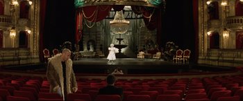 Movie still from “xXx” (2002), directed by Rob Cohen – A woman in a white dress standing in front of a chandelier on a stage; Wide shot, High angle
