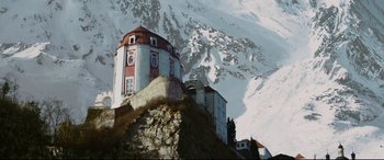 Movie still from “xXx” (2002), directed by Rob Cohen – A building on top of a hill with a snowy mountain in the background; Extreme Wide shot, Low angle