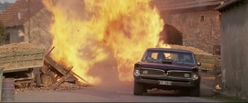 Movie still from “xXx” (2002), directed by Rob Cohen – A car is on fire in front of a building; Wide shot, High angle