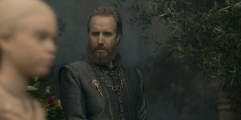 Movie still from “House of the Dragon” (2022), created by George R.R. Martin – A man with long hair and a beard wearing chains; Medium shot, Over the shoulder angle