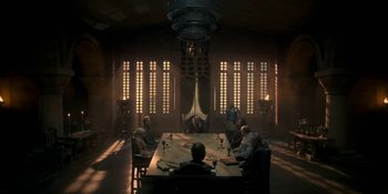 Movie still from “House of the Dragon” (2022), created by George R.R. Martin – A group of people sitting around a table in a room; Wide shot, Low angle