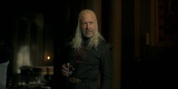 Movie still from “House of the Dragon” (2022), created by George R.R. Martin – A man with long white hair holding a drink; Medium shot, Over the shoulder angle