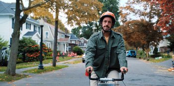 Movie still from “Hubie Halloween” (2020), directed by Steven Brill – A man riding a bicycle down a street; Wide shot, Over the shoulder angle