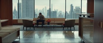 Movie still from “Human Capital” (2019), directed by Marc Meyers – A man sitting on top of a couch in front of a window; Extreme Wide shot, Low angle