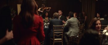 Movie still from “Human Capital” (2019), directed by Marc Meyers – A group of people sitting around a table with a violin; Wide shot, Over the shoulder angle