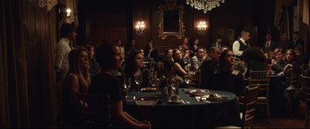 Movie still from “Human Capital” (2019), directed by Marc Meyers – A group of people sitting at a table in front of a mirror; Wide shot, Over the shoulder angle