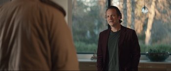 Movie still from “Human Capital” (2019), directed by Marc Meyers – A man standing in front of a window looking at the camera; Medium shot, Over the shoulder angle