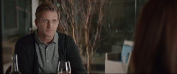 Movie still from “Human Capital” (2019), directed by Marc Meyers – A man sitting at a table with a glass of wine; Medium shot, Over the shoulder angle