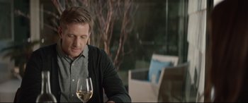 Movie still from “Human Capital” (2019), directed by Marc Meyers – A person sitting at a table with a glass of wine; Medium shot, Over the shoulder angle