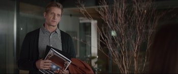 Movie still from “Human Capital” (2019), directed by Marc Meyers – A man holding a laptop and a book in his hands; Medium shot, Over the shoulder angle