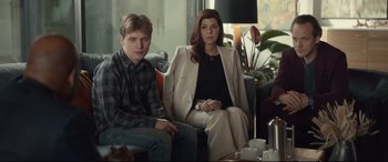 Movie still from “Human Capital” (2019), directed by Marc Meyers – A man and a woman sitting on a couch in front of a window; Medium shot, High angle