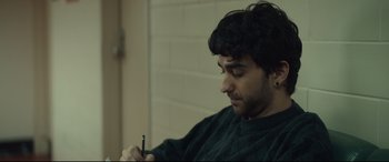 Movie still from “Human Capital” (2019), directed by Marc Meyers – A young man holding a cell phone in his hand; Close Up shot, Over the shoulder angle