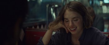 Movie still from “Human Capital” (2019), directed by Marc Meyers – A young woman smiling while sitting in a chair; Close Up shot, Over the shoulder angle