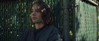 Movie still from “Human Capital” (2019), directed by Marc Meyers – A young woman with short brown hair wearing a black jacket; Close Up shot, Low angle