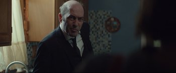 Movie still from “Human Capital” (2019), directed by Marc Meyers – An older bald man in a suit and tie; Close Up shot, Over the shoulder angle