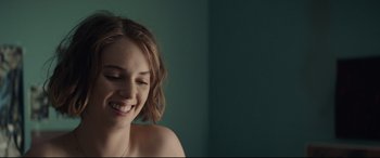 Movie still from “Human Capital” (2019), directed by Marc Meyers – A young woman smiles while posing for a picture; Close Up shot, Over the shoulder angle