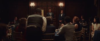 Movie still from “Human Capital” (2019), directed by Marc Meyers – A group of people sitting at a table in a room; Medium shot, Over the shoulder angle