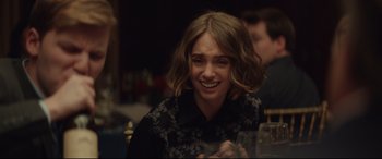 Movie still from “Human Capital” (2019), directed by Marc Meyers – A young woman smiles while sitting at a dinner table; Close Up shot, Over the shoulder angle