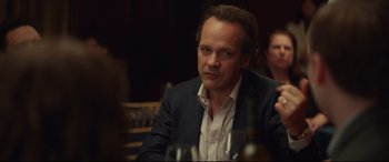 Movie still from “Human Capital” (2019), directed by Marc Meyers – A man sitting at a table with a bottle of wine in front of him; Close Up shot, Over the shoulder angle