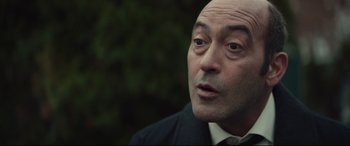 Movie still from “Human Capital” (2019), directed by Marc Meyers – A man in a suit and tie looking at the camera; Close Up shot, Over the shoulder angle