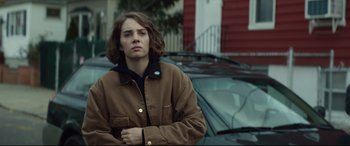 Movie still from “Human Capital” (2019), directed by Marc Meyers – A woman standing in front of a parked car on the side of the road; Close Up shot, Over the shoulder angle
