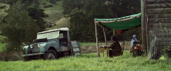 Movie still from “Hunt for the Wilderpeople” (2016), directed by Taika Waititi – A man sitting at a table in the grass next to an old truck; Wide shot, Low angle