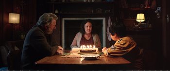Movie still from “Hunt for the Wilderpeople” (2016), directed by Taika Waititi – A woman sitting in front of a birthday cake with lit candles on it; Medium shot, Over the shoulder angle