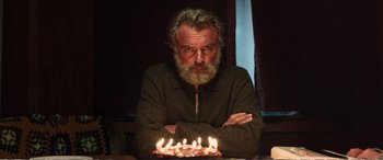Movie still from “Hunt for the Wilderpeople” (2016), directed by Taika Waititi – An older man sitting in front of a cake with lit candles; Medium shot, High angle