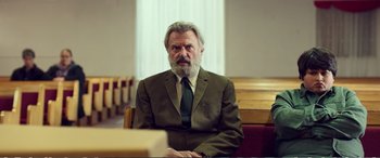 Movie still from “Hunt for the Wilderpeople” (2016), directed by Taika Waititi – An older man in a suit sitting in front of a window; Medium shot, Low angle