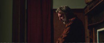 Movie still from “Hunt for the Wilderpeople” (2016), directed by Taika Waititi – A man with long hair and a beard standing in front of a red curtain; Medium shot, Low angle