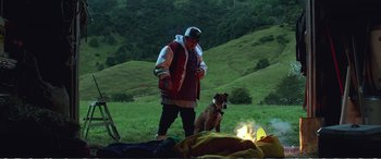 Movie still from “Hunt for the Wilderpeople” (2016), directed by Taika Waititi – A man standing next to a dog next to a campfire; Wide shot, Low angle