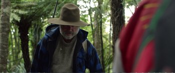 Movie still from “Hunt for the Wilderpeople” (2016), directed by Taika Waititi – An older man with a hat and a backpack in the woods; Medium shot, Over the shoulder angle