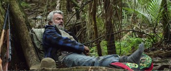 Movie still from “Hunt for the Wilderpeople” (2016), directed by Taika Waititi – An older man sitting on the ground in the woods; Medium shot, Low angle