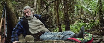 Movie still from “Hunt for the Wilderpeople” (2016), directed by Taika Waititi – An older man sitting on the ground next to a forest; Wide shot, High angle