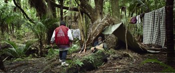 Movie still from “Hunt for the Wilderpeople” (2016), directed by Taika Waititi – A man in a red jacket is standing in the woods; Wide shot, Over the shoulder angle