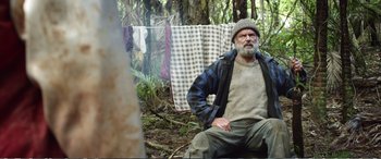 Movie still from “Hunt for the Wilderpeople” (2016), directed by Taika Waititi – An older man sitting in the woods next to a clothesline; Medium shot, Low angle
