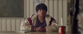 Movie still from “Hunt for the Wilderpeople” (2016), directed by Taika Waititi – A young man sitting at a table with his hands crossed; Close Up shot, Over the shoulder angle