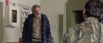 Movie still from “Hunt for the Wilderpeople” (2016), directed by Taika Waititi – An older man wearing a plaid shirt and a brown sweater; Medium shot, Over the shoulder angle