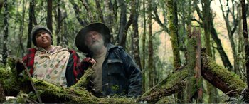 Movie still from “Hunt for the Wilderpeople” (2016), directed by Taika Waititi – A man in a hat and jacket standing next to a tree; Medium shot, Low angle