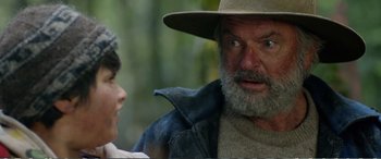Movie still from “Hunt for the Wilderpeople” (2016), directed by Taika Waititi – An old man with a beard and a hat is talking to a young boy; Close Up shot, Over the shoulder angle