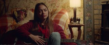 Movie still from “Hunt for the Wilderpeople” (2016), directed by Taika Waititi – A woman sitting in a chair holding a guitar; Medium shot, Over the shoulder angle