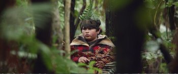 Movie still from “Hunt for the Wilderpeople” (2016), directed by Taika Waititi – A young boy in the woods wearing a hat and jacket; Medium shot, Over the shoulder angle