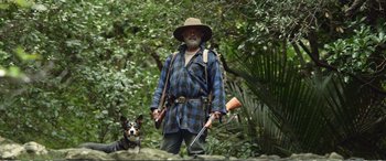 Movie still from “Hunt for the Wilderpeople” (2016), directed by Taika Waititi – A man and a dog are walking in the woods; Medium shot, Low angle