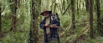 Movie still from “Hunt for the Wilderpeople” (2016), directed by Taika Waititi – An older man holding a rifle in the woods; Medium shot, Low angle