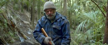 Movie still from “Hunt for the Wilderpeople” (2016), directed by Taika Waititi – An old man holding a rifle in the woods; Medium shot, Over the shoulder angle