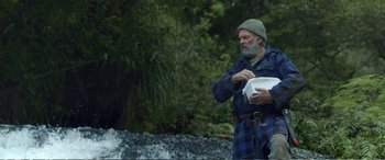 Movie still from “Hunt for the Wilderpeople” (2016), directed by Taika Waititi – An older man holding a bucket near a waterfall; Medium shot, Low angle